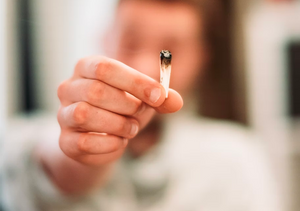 man holding a joint that needs to be ashed into an ashtray 